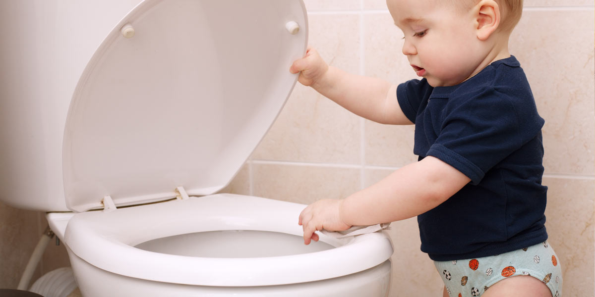 Toddler looking in toilet. Children's toys are often the cause of a clogged toilet.